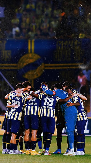 Fenerbahce players huddle together on the pitch during a rainy night match HD phone wallpaper