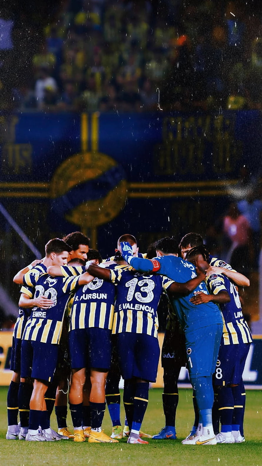 Fenerbahce players huddle together on the pitch during a rainy night match HD phone wallpaper