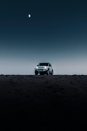 Land Rover Defender SUV on a dark desert ridge under a crescent moon at night HD phone wallpaper