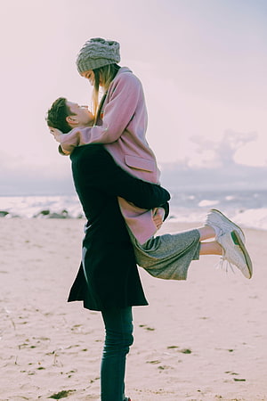 Romantic couple embracing on a sandy beach with ocean waves in the background HD phone wallpaper