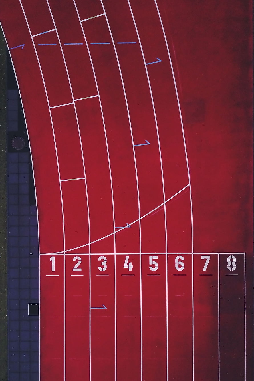 Aerial View of Red Athletics Track with Numbered Lanes and Start Line HD phone wallpaper