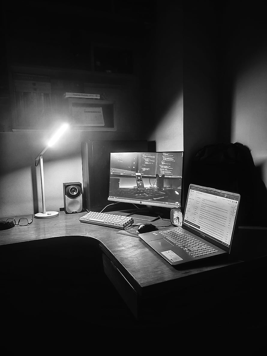 Monochrome Developer Workspace Featuring Laptop, Monitor, and Desk Lamp in a Dark Room HD phone wallpaper