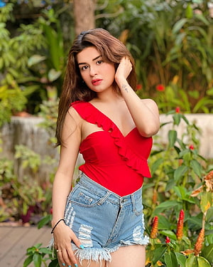 Avneet Kaur in a red ruffled top and distressed denim shorts in a lush garden HD phone wallpaper