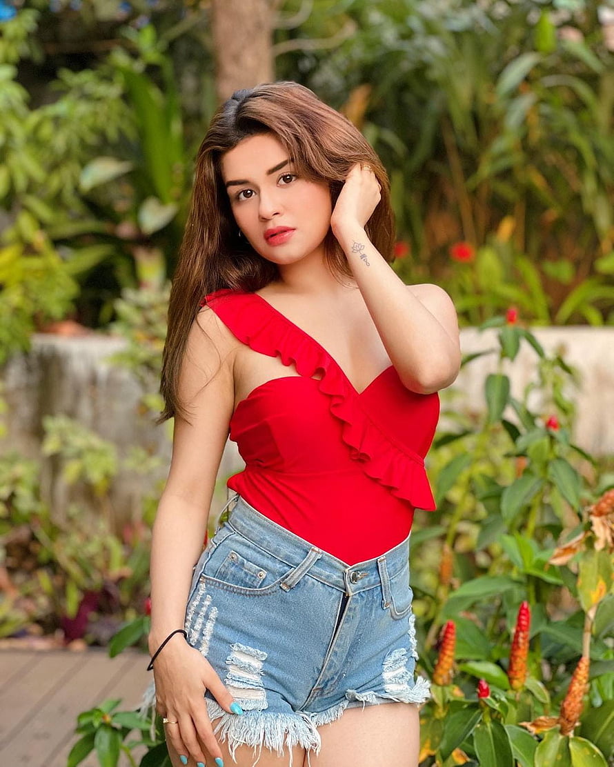 Avneet Kaur in a red ruffled top and distressed denim shorts in a lush garden HD phone wallpaper