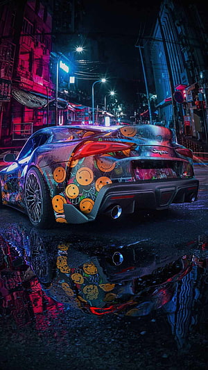 Custom Toyota Supra with smiley face wrap parked on a wet neon-lit city street at night HD phone wallpaper