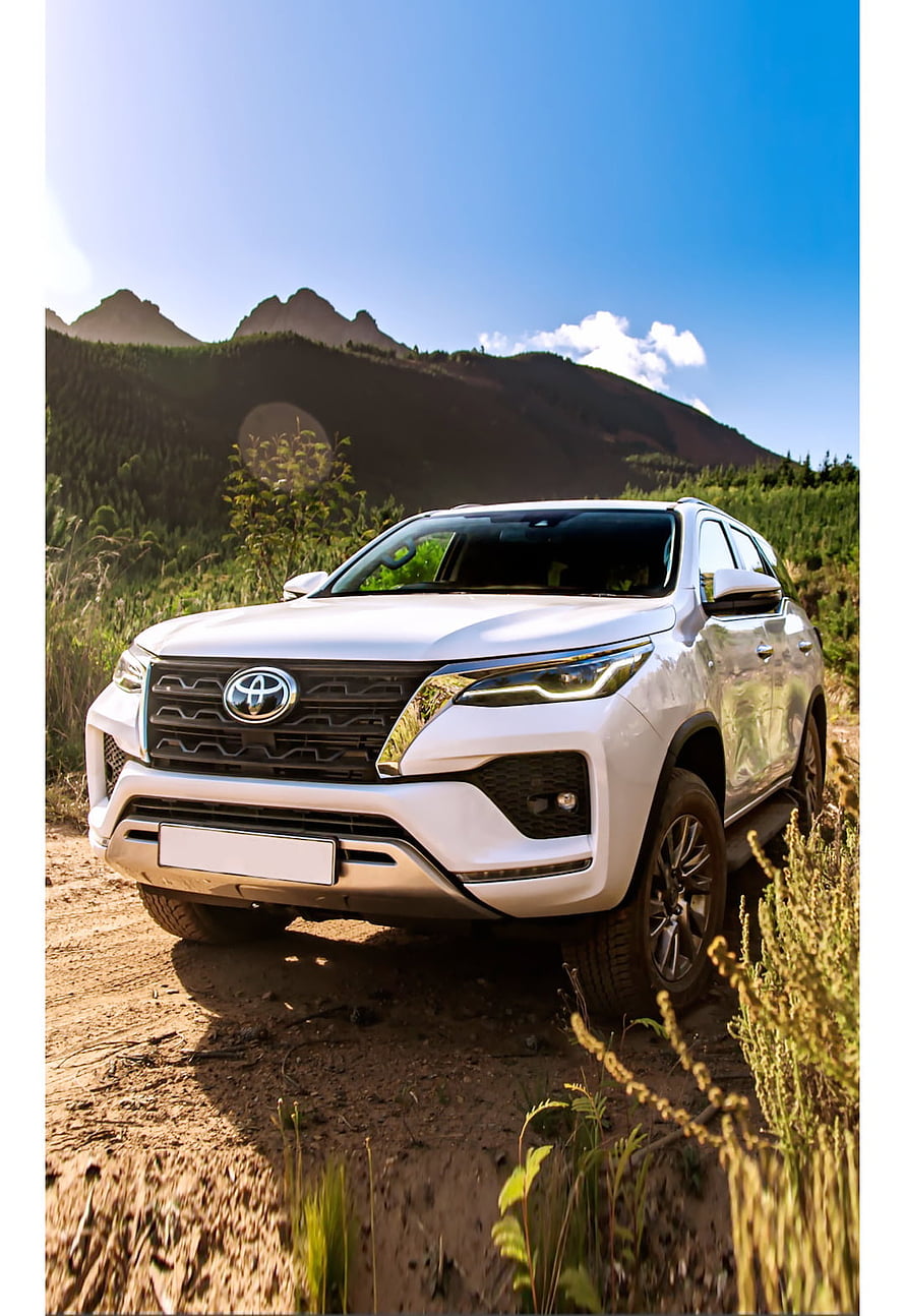 White Toyota Fortuner SUV on a dirt trail with mountain backdrop under a clear blue sky HD phone wallpaper