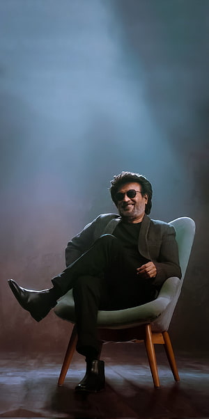 Rajinikanth in a moody studio portrait wearing sunglasses and a dark jacket seated in a modern chair HD phone wallpaper