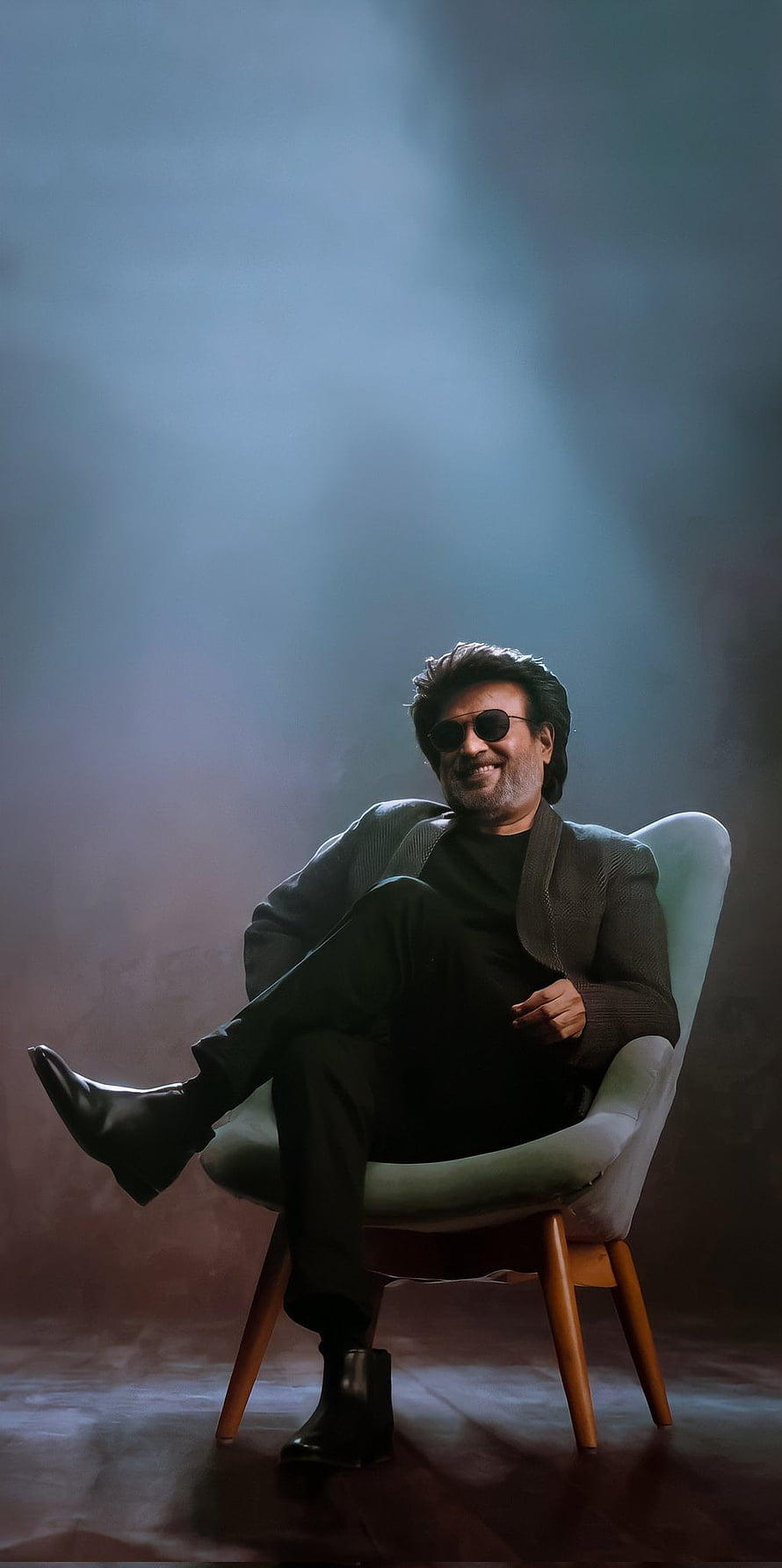 Rajinikanth in a moody studio portrait wearing sunglasses and a dark jacket seated in a modern chair HD phone wallpaper