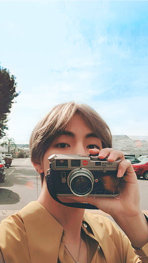 V BTS Holding Vintage Leica Camera in Sunlit Outdoor Setting HD phone wallpaper