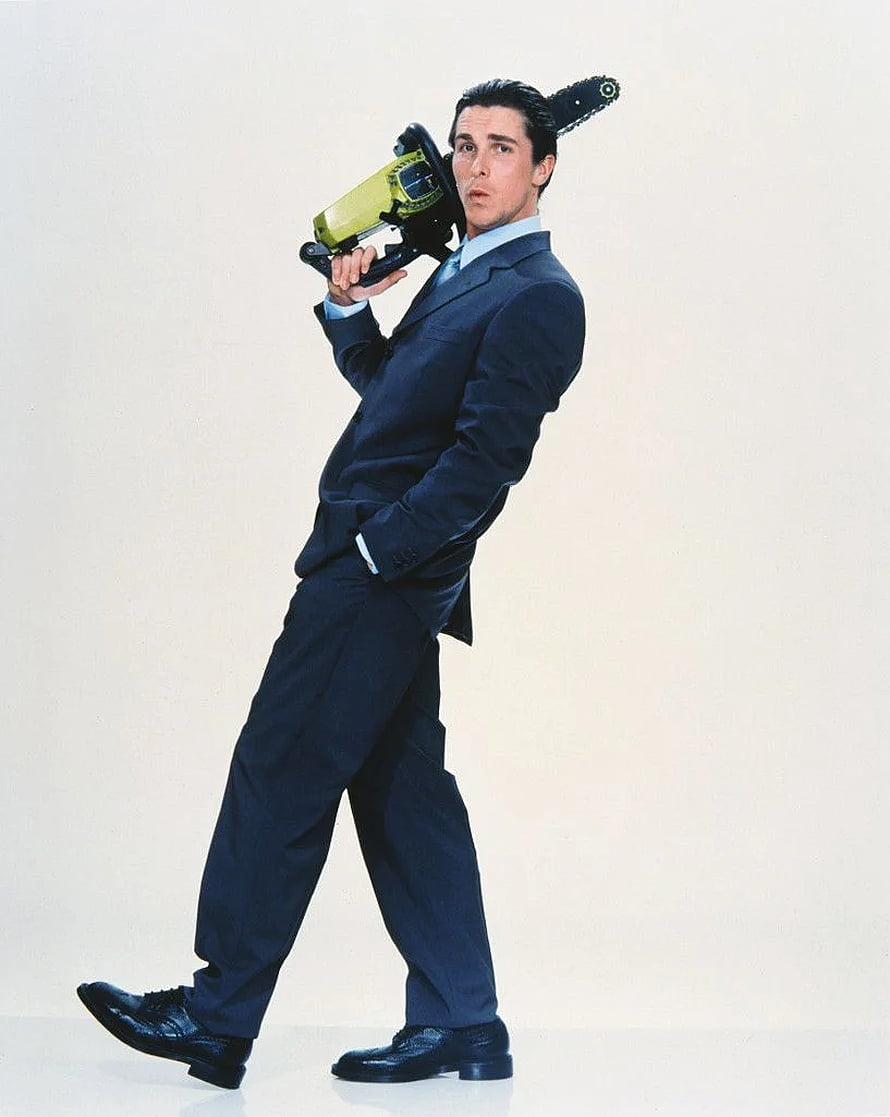 Christian Bale as Patrick Bateman in American Psycho holding a chainsaw in a dark suit HD phone wallpaper