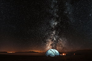 Illuminated Camping Tent Under the Milky Way Galaxy in a Dark Desert Landscape HD wallpaper