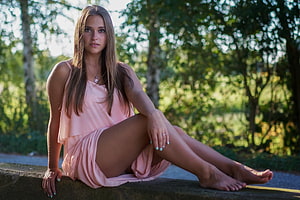 Young woman in a flowing pink dress sitting barefoot on a stone ledge in a sunlit forest, Brunette, Girl, Beautiful, Beauty, Woman, Model, Lovely, Female HD wallpaper