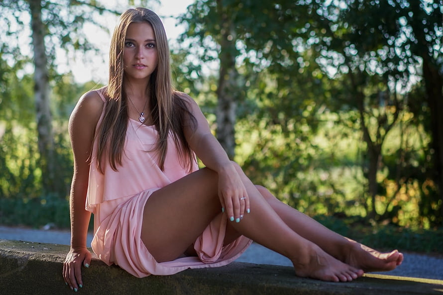 Young woman in a flowing pink dress sitting barefoot on a stone ledge in a sunlit forest, Brunette, Girl, Beautiful, Beauty, Woman, Model, Lovely, Female HD wallpaper
