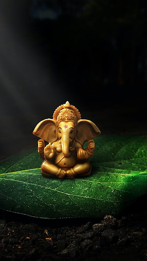 Golden Ganesha Idol Seated on a Large Green Leaf in Dramatic Low-Key Lighting HD phone wallpaper