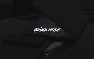 Dark Minimalist Desk Setup With Laptop And Smartphone Featuring Grind Mode Typography HD wallpaper