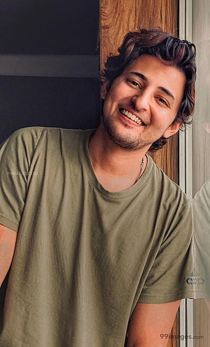 Darshan Raval smiling portrait in olive green t-shirt leaning against wooden door frame HD phone wallpaper