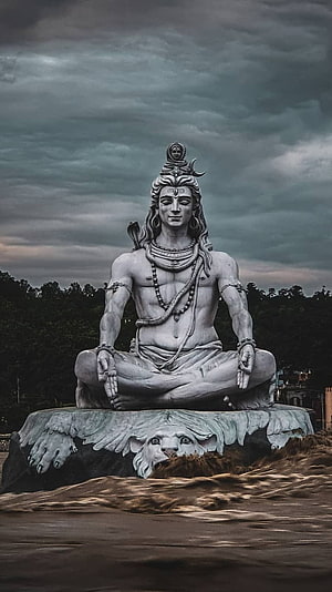 Meditating Shiva Statue Seated on Eagle Pedestal Under Dramatic Stormy Sky HD phone wallpaper