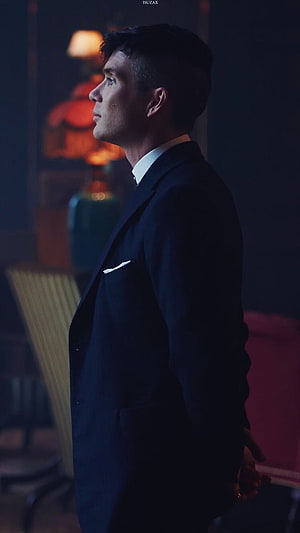 Finn Shelby in a dark suit standing in a dimly lit room with warm ambient lighting HD phone wallpaper