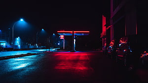 Neon-lit gas station at night with red and blue street reflections on wet asphalt HD wallpaper