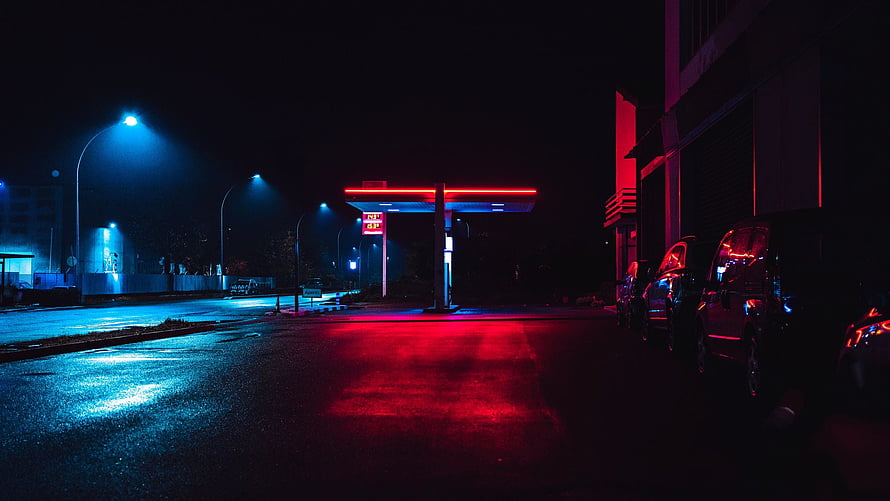 Neon-lit gas station at night with red and blue street reflections on wet asphalt HD wallpaper