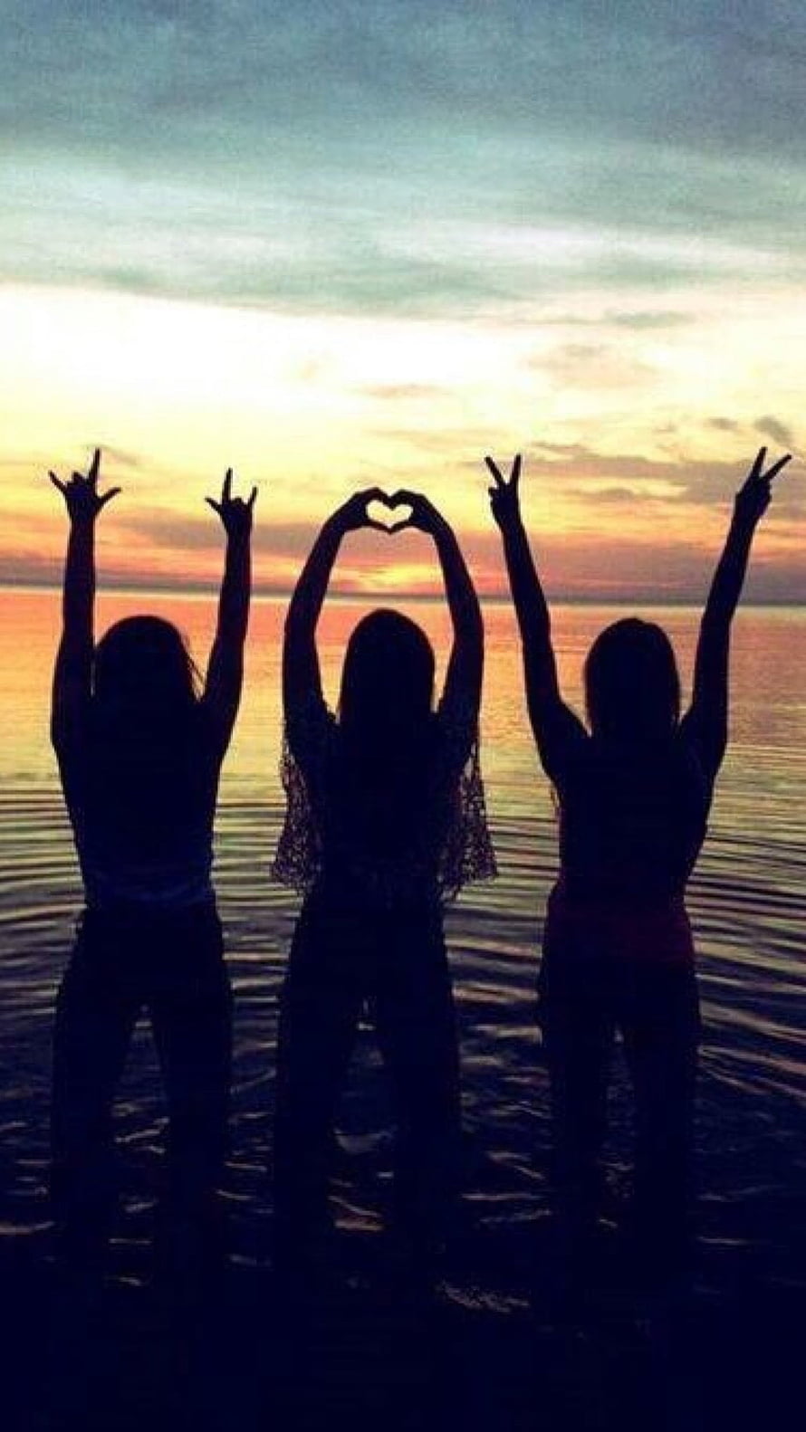 Three friends silhouetted against a vibrant sunset over the ocean making peace and heart signs HD phone wallpaper