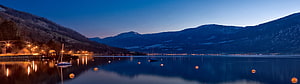 Serene Alpine Lake at Dusk with Mountain Reflections and Warm Shoreline Lights HD wallpaper